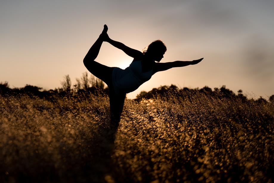 Pregnant expectant mother performing yoga pose in golden grassy field silhouetted against the setting sun