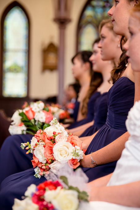 Bridesmaids sitting in a row in the pews with their bouquets looking at bride and groom during ceremony