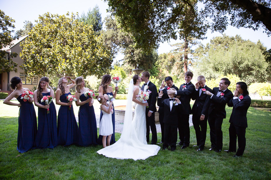 Bride and groom kissing while the bridal party covers their eyes and looks away