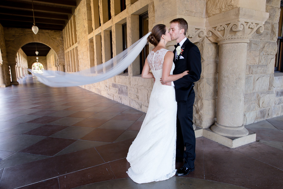 Groom kissing bride with veil blowing in the wind at Stanford Main Quad
