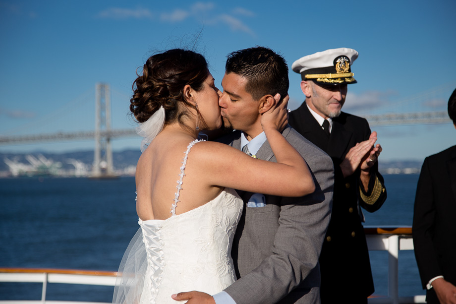 Bride and groom kissing after their marriage ceremony with the captain clapping