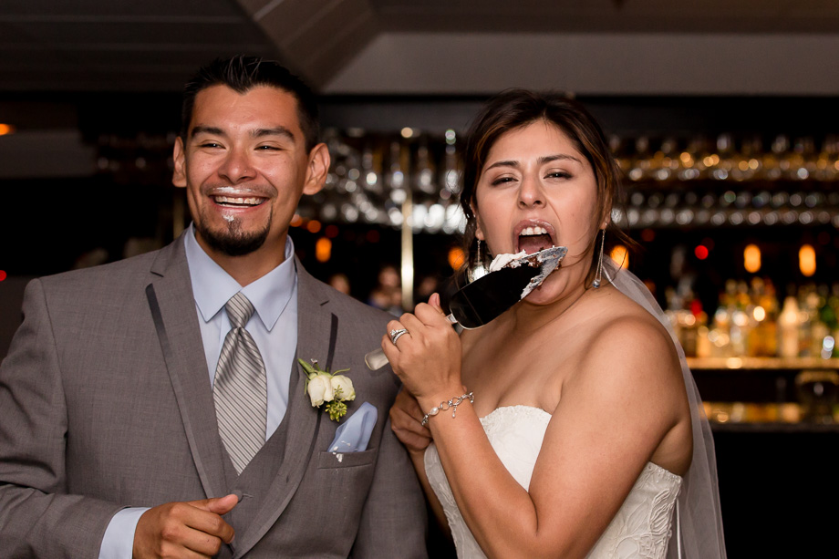 Bride licking the wedding cake knife, groom with cake smeared on his mouth
