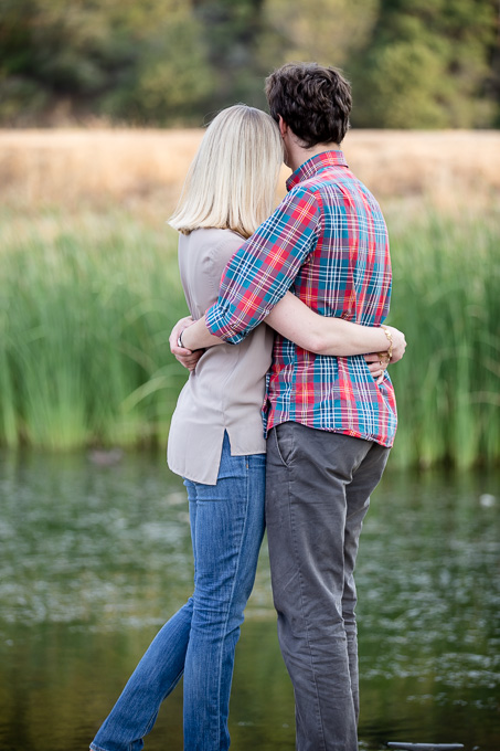 Hugging couple looking away from the camera into grass across the lake