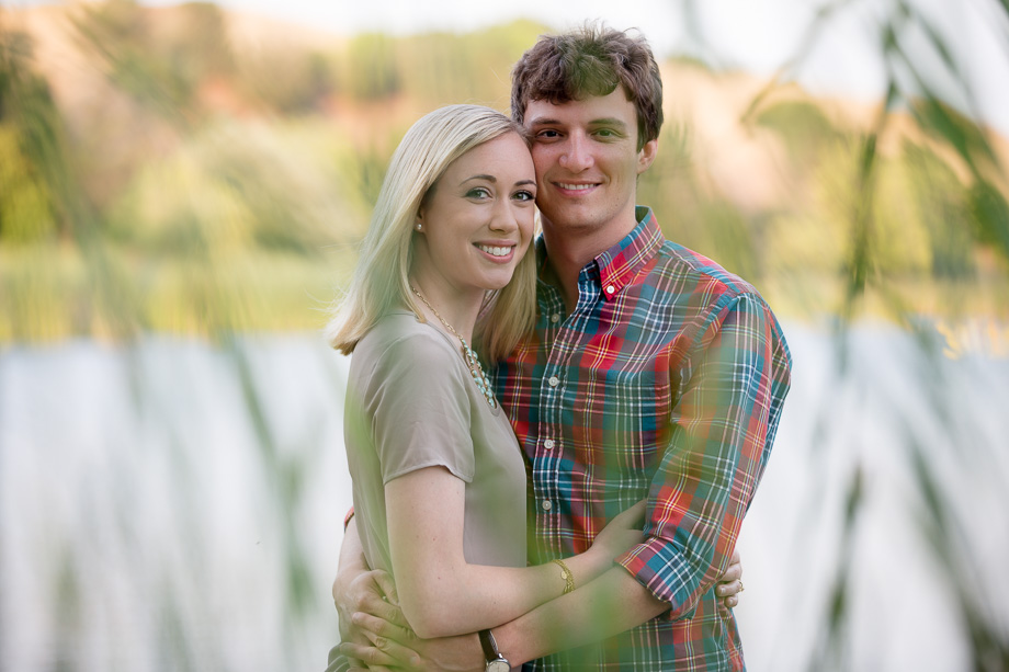 Couple standing in front of a lake with some shubbery in front