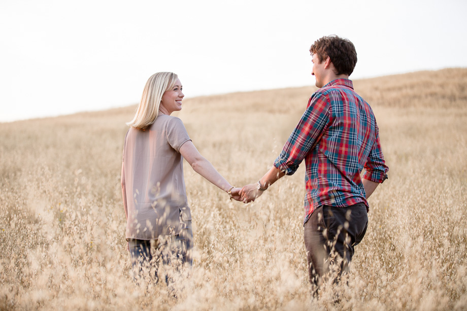 Newly engaged couple holding hands and walking in a beautiful yellow grassy field