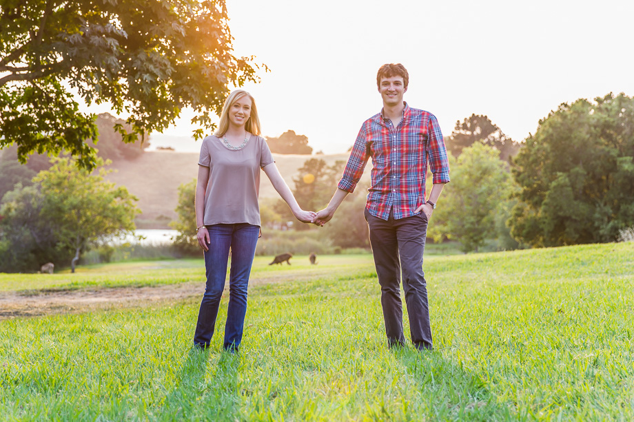 Engagement photo of couple standing under the evening sunset with deer in the background