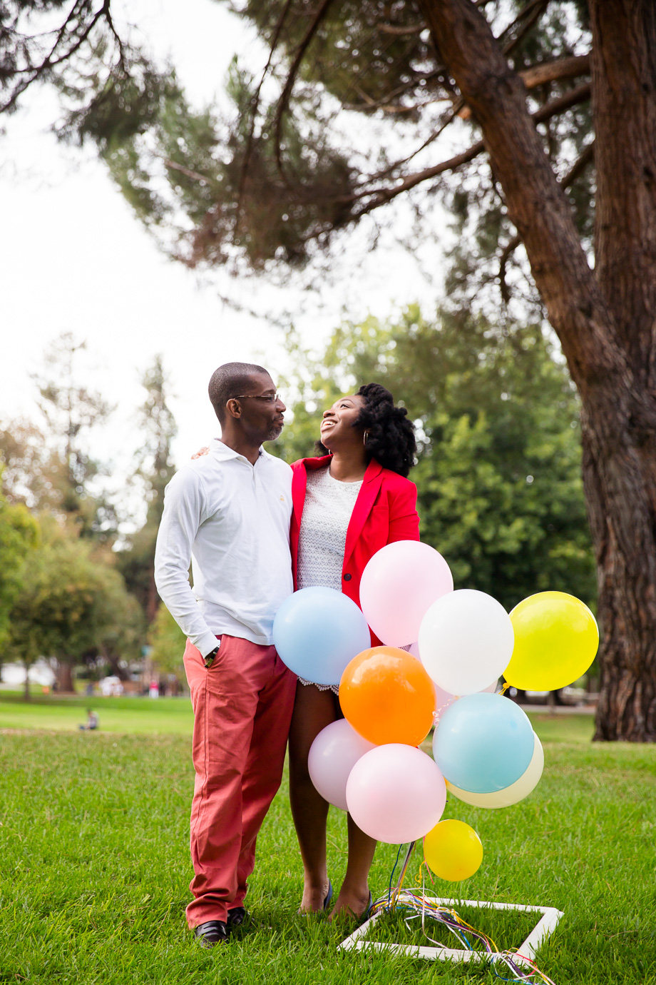 anniversary photo of couple laughing behind a bunch of colorful balloons