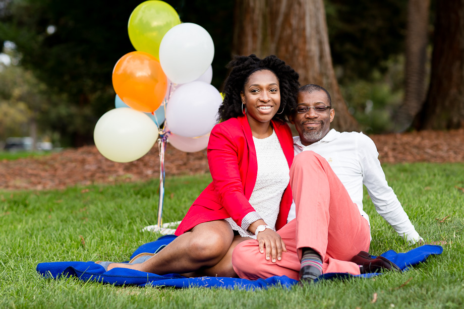 couple sitting on picnic blanket in front of balloons for anniversary picture
