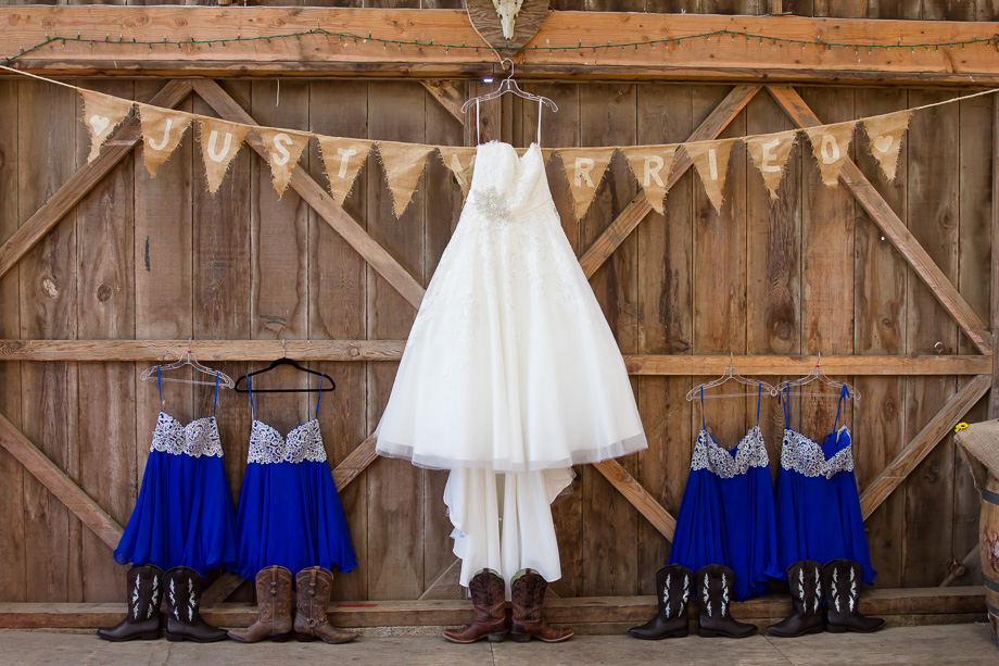 Wedding gown and bridesmaid dresses and boots hanging in barn