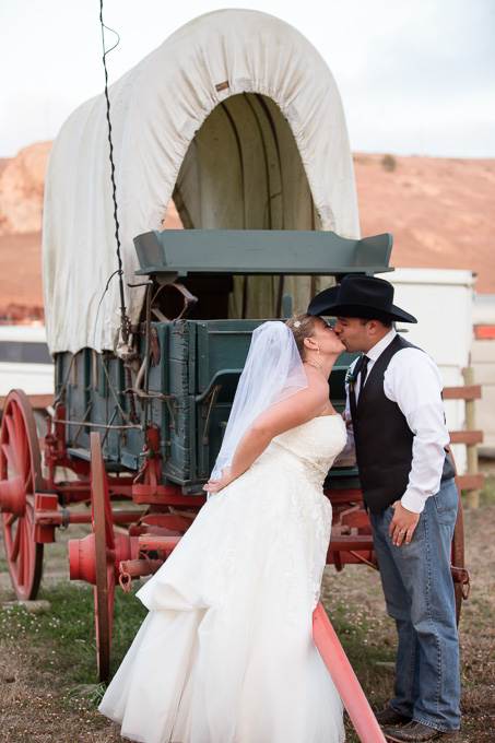 Bride and groom kissing in front of an old horse wagon at Chanslor Ranch