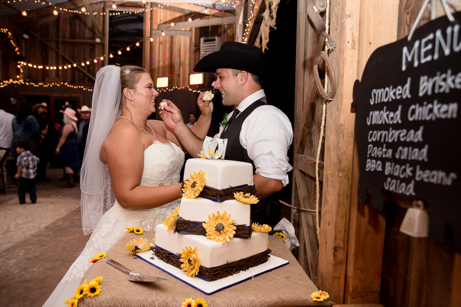 Bride and groom feeding each other cake indoors at the barn