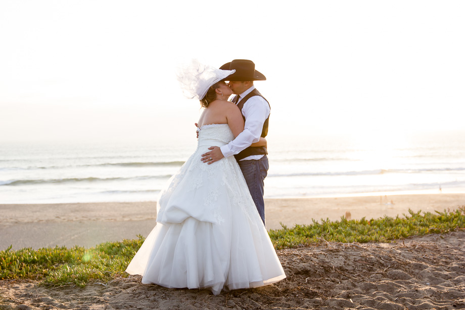 Bride and groom kissing in front of a beach sunset backdrop