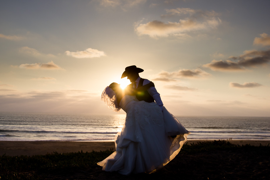 Silhouette photo of the dip by bride and groom at an ocean beach sunset