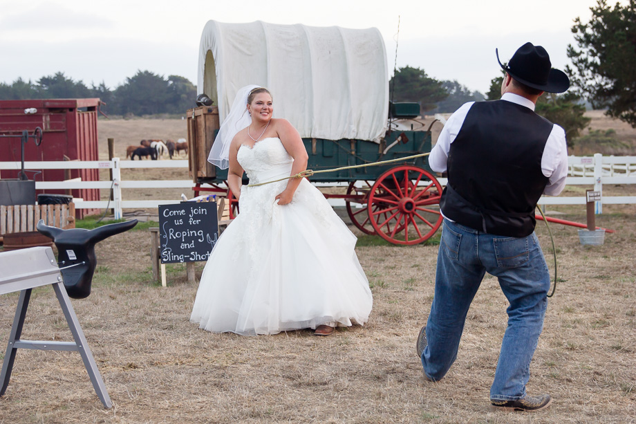 Groom lassoing the bride in front of a wagon at a country wedding