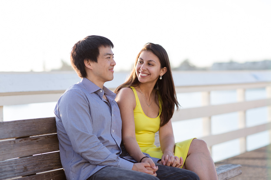engaged couple sitting on a pier bench holding hands