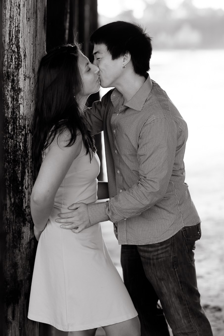 newly engaged couple kissing by the pillars on the beach underneath the Santa Cruz Wharf pier