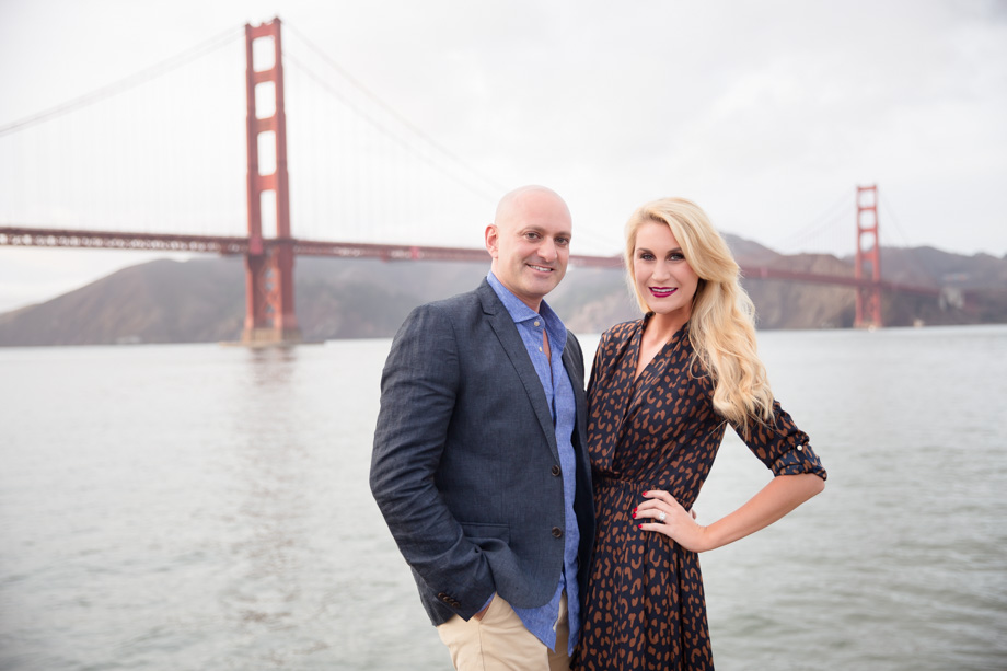 portrait photo of couple standing on the shore of the San Francisco Bay in front of the span of the Golden Gate Bridge