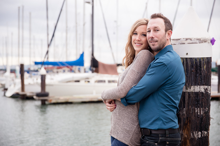 romantic engagement photo at the end of a pier in front of docked boats