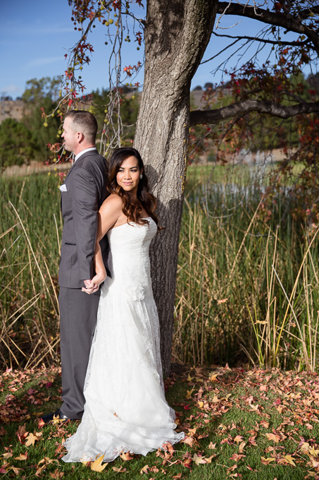 couple standing back-to-back and holding hands under a tree just before their wedding ceremony