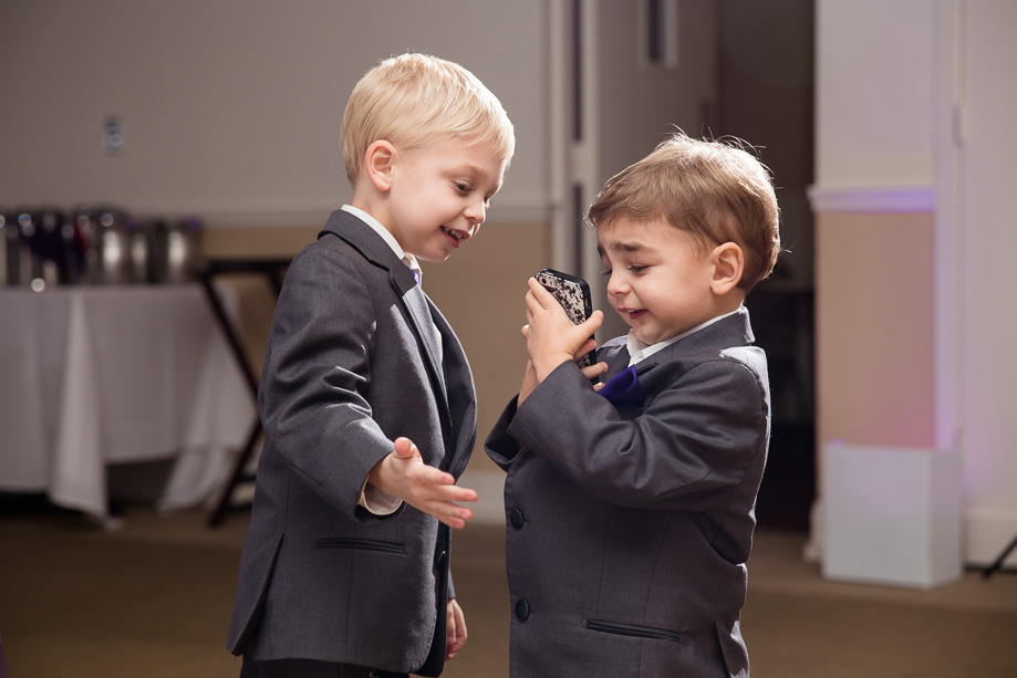 little kids suited up at wedding and playing with a cell phone in the reception hall