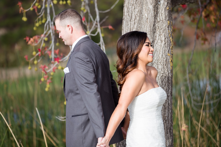 bride and groom holding hands back to back under a tree before first look