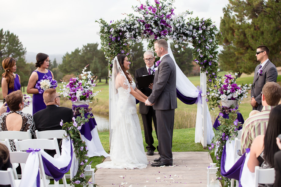 Happy couple tying the knot under a purple arch at the Boundary Oak Golf Club
