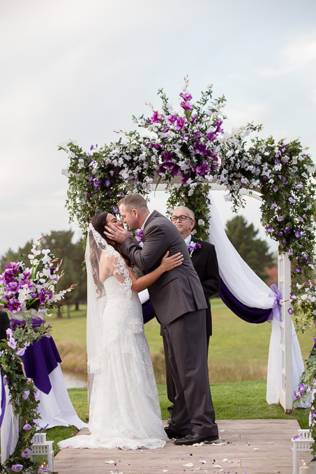 Happy couple kissing each other as husband and wife under a purple arch at the Boundary Oak Golf Club
