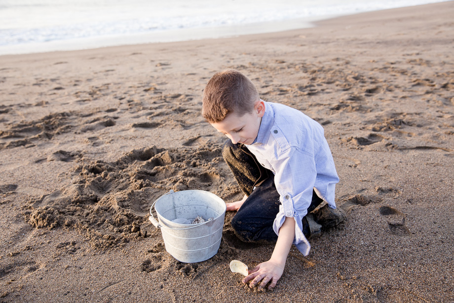 five year old boy playing sand with seashells on beaker beach