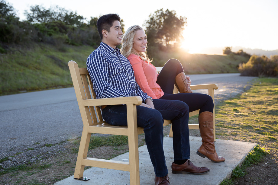 engagement photo of a couple sitting on a beanch during sunset