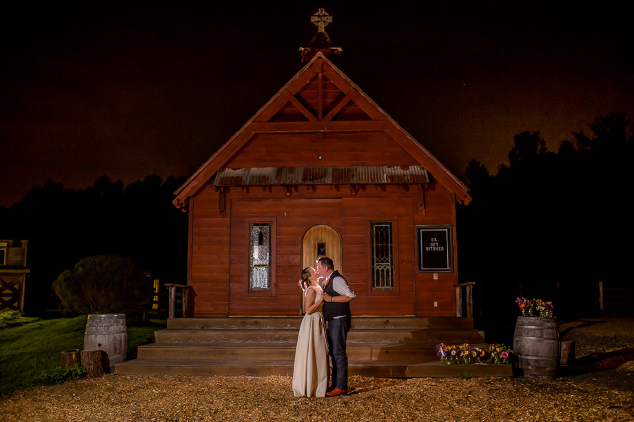dramatic night shot of the bride and groom in front of the red chapel at long branch
