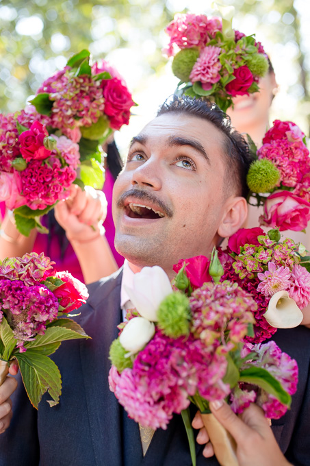 bold colored portrait of the groom framed by bridesmaids bouquets