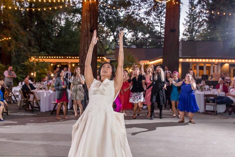 bride tossing bouquet under string lights
