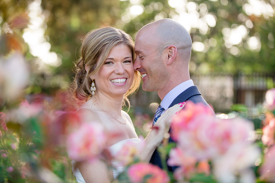bride and groom behind flowers in rose garden