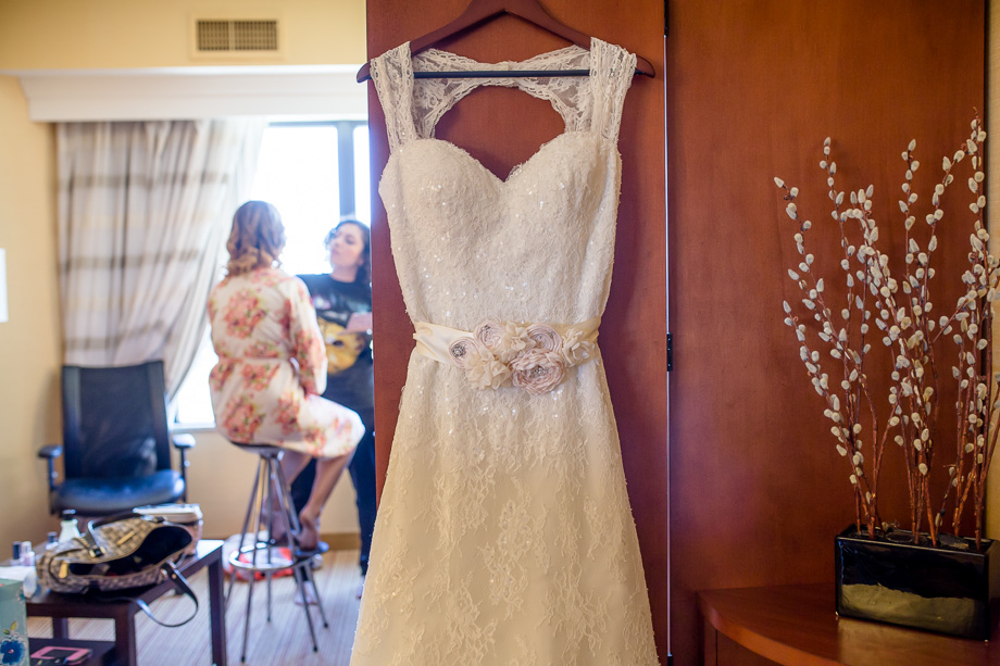 bride's dress hanging on door while she gets her makeup done