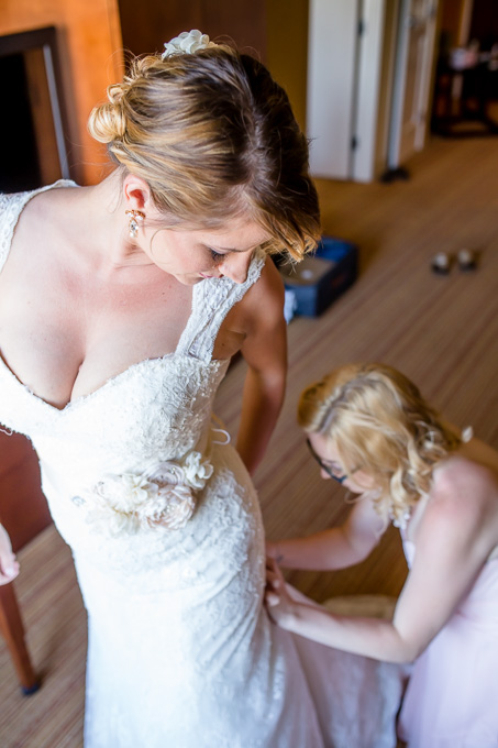 bridesmaid helping bride put on her dress