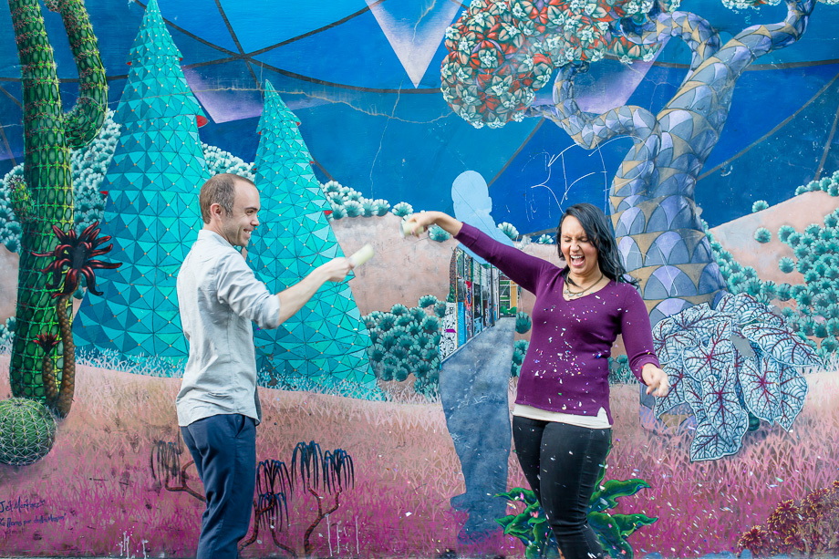 fun confetti fight engagement photo in front of san francisco colorful mural