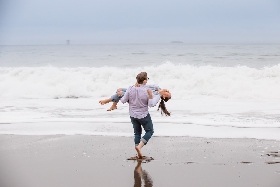 playful baker beach engagement photo - couple run toward the huge tide