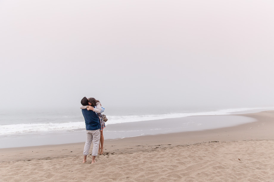 couple embracing on a foggy beach after he proposed and she said yes
