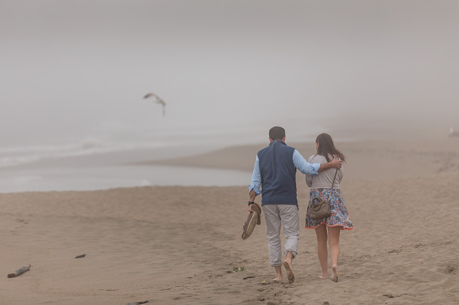 couple walking down Baker Beach with a seagull flying in the background