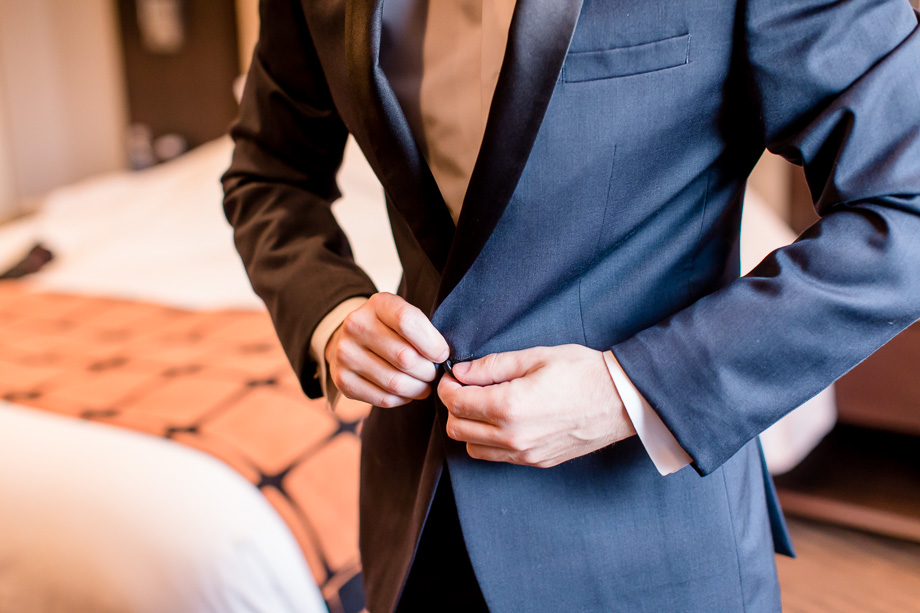 groom getting ready buttoning suit in hotel room