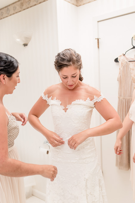 bride getting into her lace wedding dress by the help of her bridesmaids