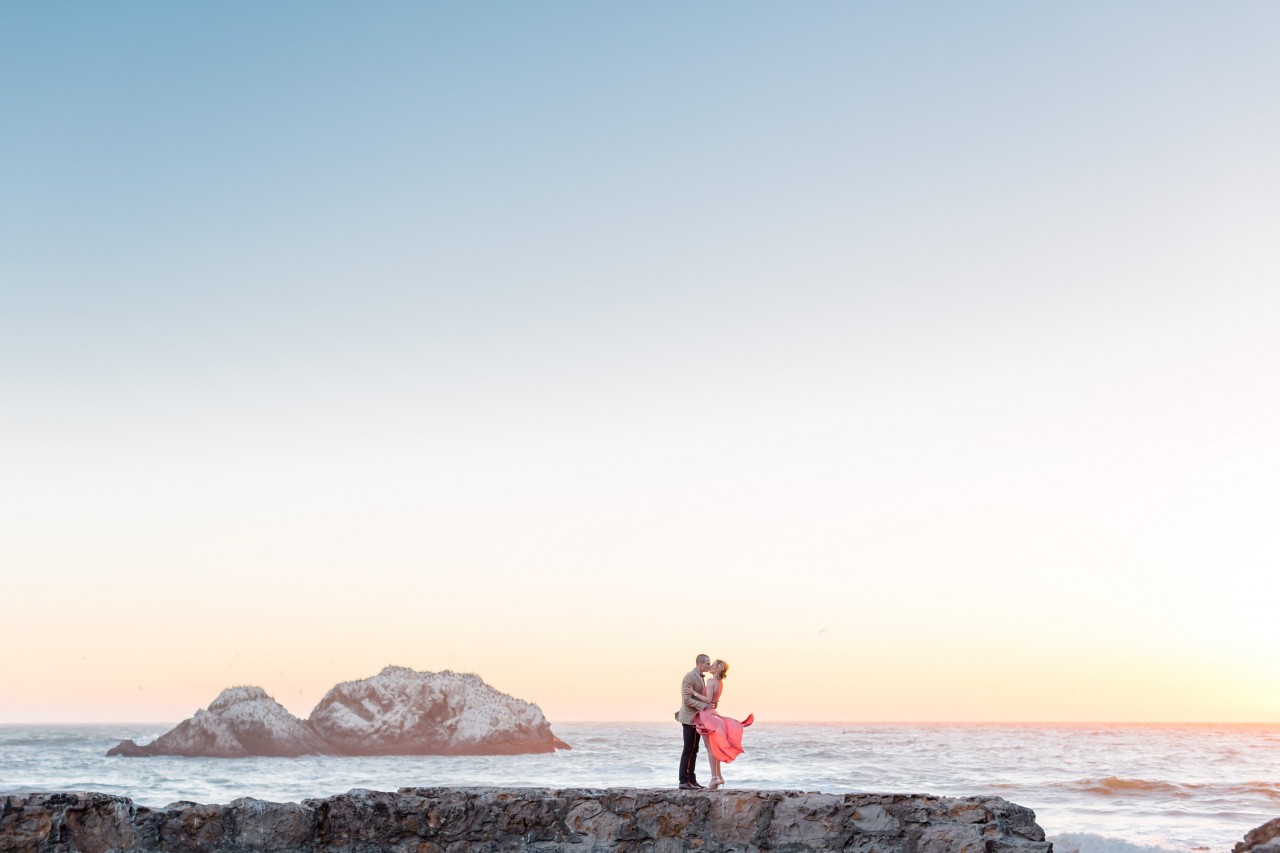 engagement photos against a pink and blue sunset sky by the ocean