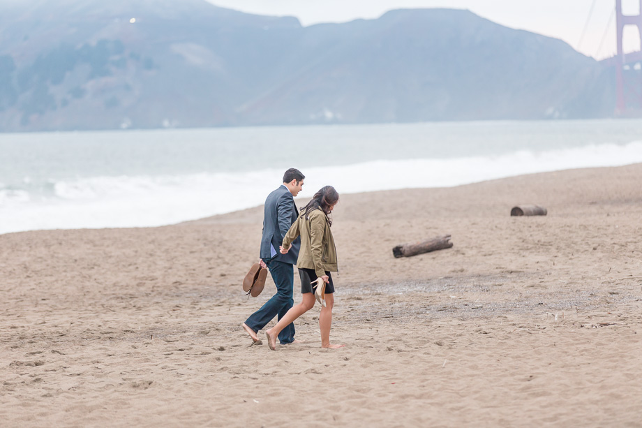 couple strolling down Baker Beach towards Golden Gate Bridge