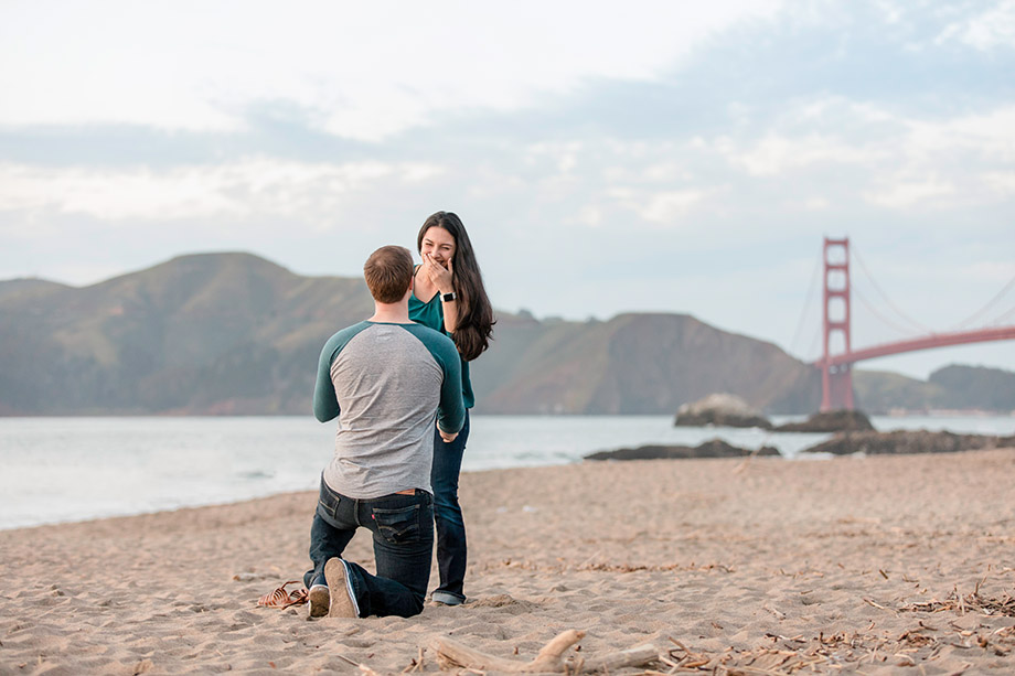 surprise marriage proposal happy reaction at Baker Beach with Golden Gate Bridge background