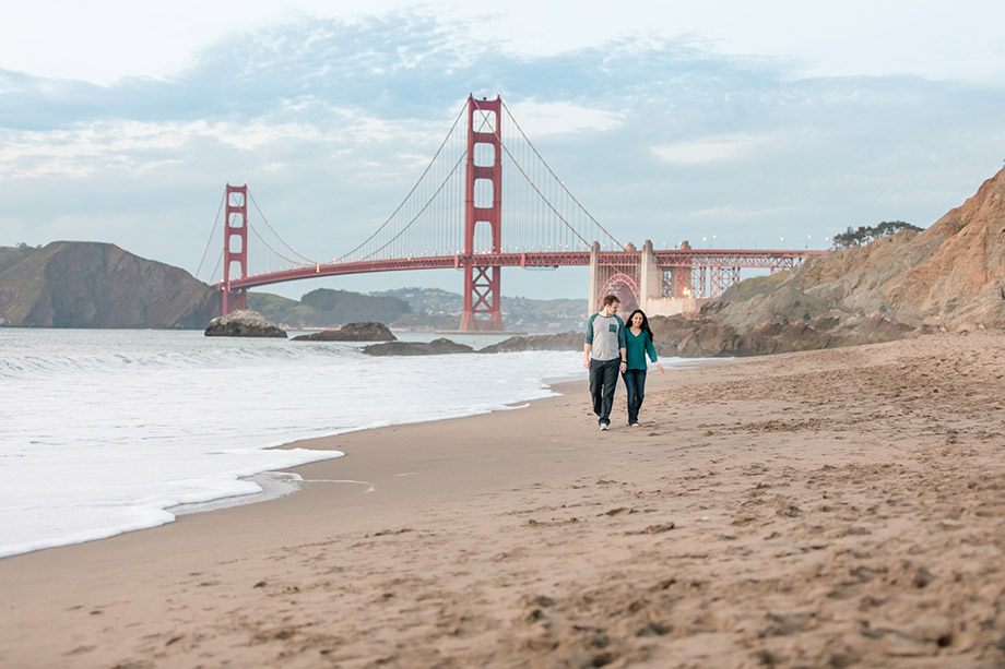 boyfriend and girlfriend walking along water sandy beach Golden Gate Bridge background