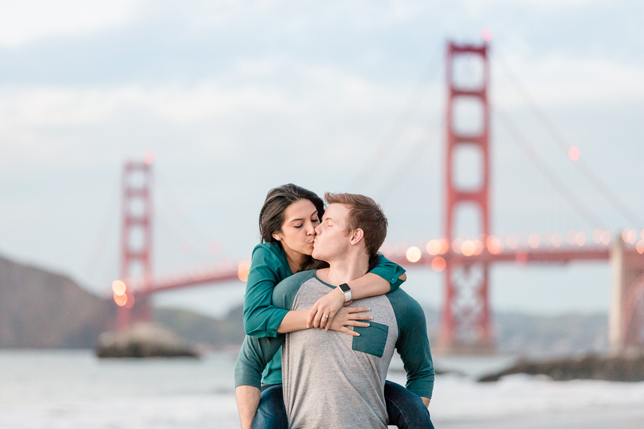 piggyback ride kiss on beach in front of Golden Gate Bridge lit at night