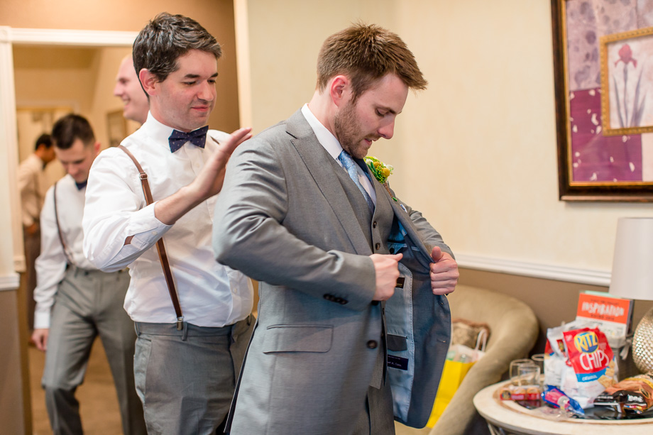 groom getting into his suit by the help of a groomsman