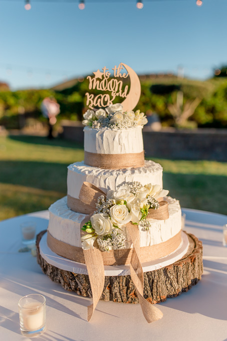 rustic wedding cake on a wooden cake stand under cafe string lights