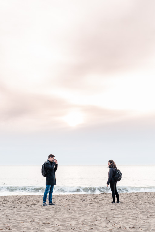 couple taking each others photos before their surprise proposal at the beach