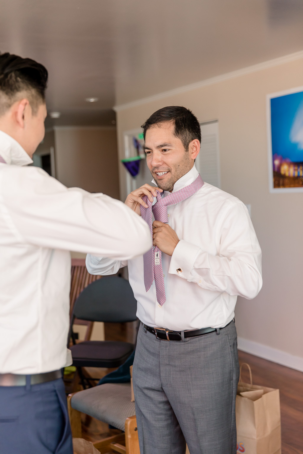 groomsman helping groom put on a tie